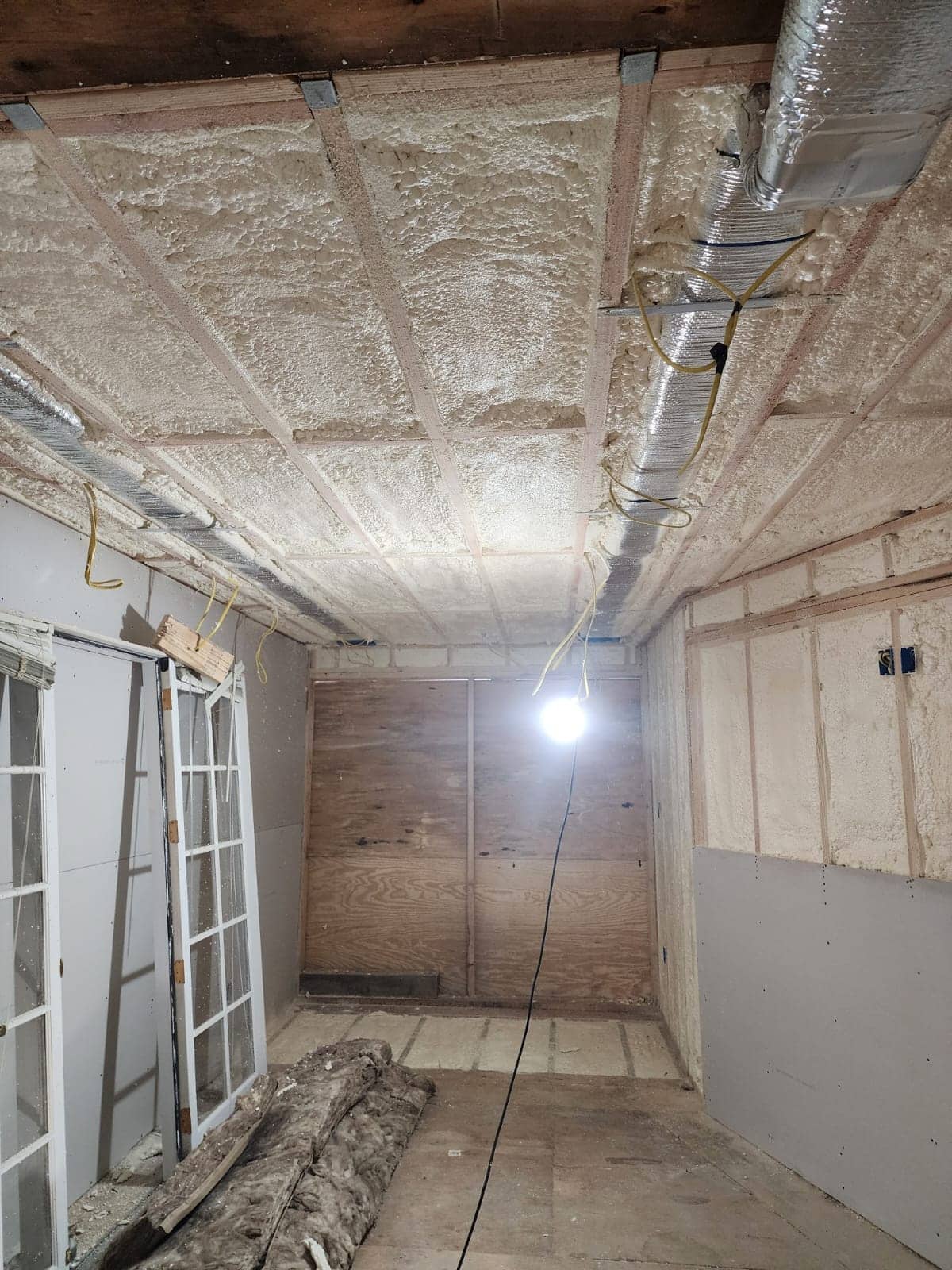 Closed cell spray foam insulation sprayed between basement ceiling joists and stud walls around ductwork and wiring